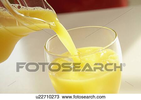 Stock Image - Orange juice pouring into glass, close up. Fotosearch