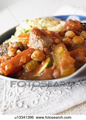 Stock Photograph - Plate of vegetables cooked in tomato sauce with couscous, close up. Fotosearch
