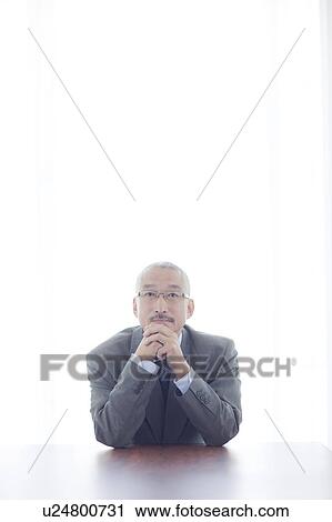 Stock Image - Portrait of businessman resting chin on hands, white background. Fotosearch