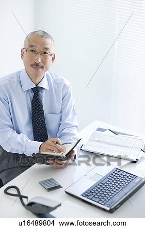 Picture - Portrait of businessman sitting at desk in office. Fotosearch