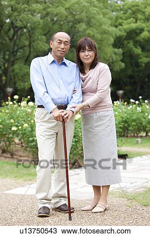 Stock Image - Portrait of mature couple in park, man holding walking stick. Fotosearch