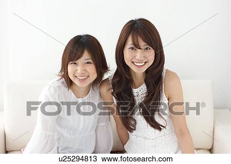 Portrait of two young women sitting on sofa, smiling View Large Photo Image Stock Image - Portrait of two young women sitting on sofa, smiling. Fotosearch