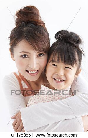 Stock Image - Portrait of woman embracing daughter, smiling, white background. Fotosearch