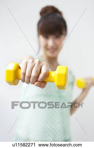 Portrait of young woman doing exercise, using dumbbells, white background, differential focus View Large Photo Image Stock Image - Portrait of young woman doing exercise, using dumbbells, white background, differential focus. Fotosearch