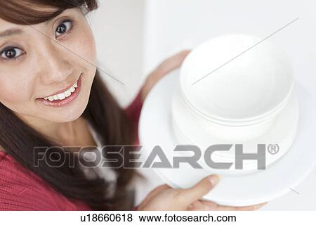 Stock Photo - Portrait of young woman holding pile of plates, close up. Fotosearch
