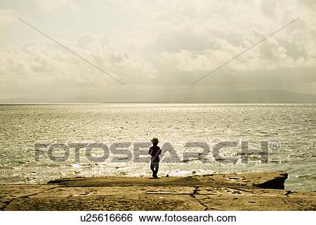 Stock Photograph - Rear view of boy standing by sea. Fotosearch