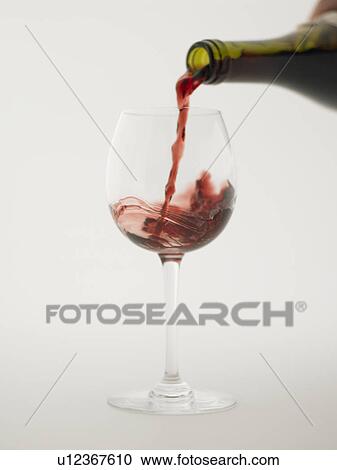 Stock Image - Red wine pouring into grass, white background. Fotosearch