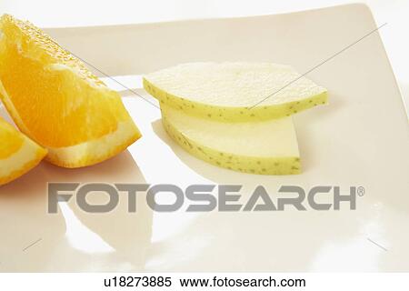 Stock Photography - Sliced orange and apple on plate, close up, white background. Fotosearch