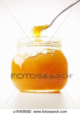 Stock Image - Spoon scooping marmalade in jar, close up, white background. Fotosearch