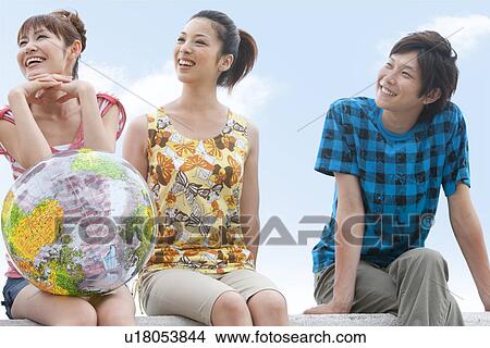 Three young people sitting on beach, woman holding beach ball View Large Photo Image Picture - Three young people sitting on beach, woman holding beach ball. Fotosearch