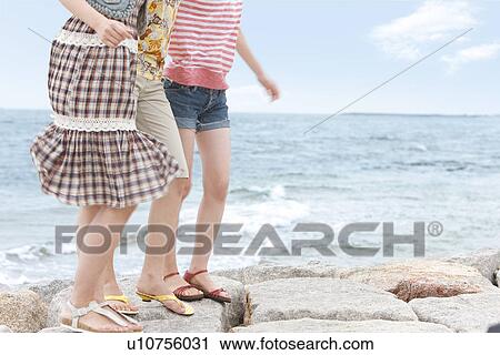 Stock Image - Three young women standing side by side at beach. Fotosearch