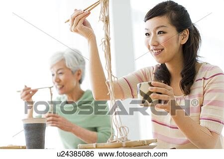 Stock Photograph - Two women eating soba noodles, smiling. Fotosearch