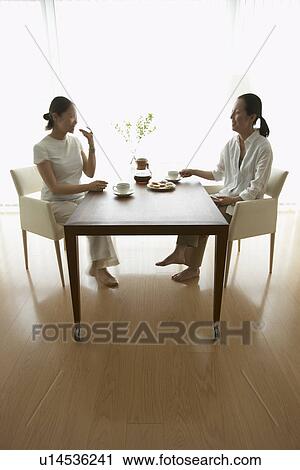 Two women sitting at table, drinking coffee View Large Photo Image Stock Image - Two women sitting at table, drinking coffee. Fotosearch
