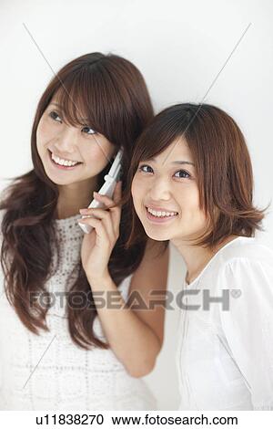 Two young women, one using mobile phone, white background View Large Photo Image Stock Image - Two young women, one using mobile phone, white background. Fotosearch