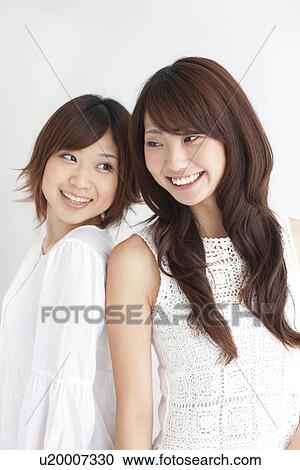 Two young women standing back to back, white background View Large Photo Image Stock Image - Two young women standing back to back, white background. Fotosearch