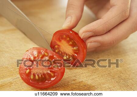Stock Photo - Woman cutting cherry tomato, close up. Fotosearch