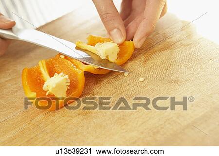 Stock Image - Woman cutting orange bell pepper, close up. Fotosearch