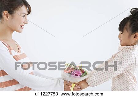 Stock Image - Woman giving flower bouquet to daughter, white background. Fotosearch