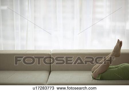 Stock Image - Woman Lying on Sofa, Feet In Air, Low Section. Fotosearch