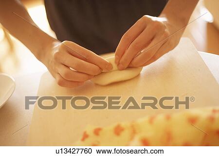 Stock Image - Woman making bagels, rolling dough, close up. Fotosearch