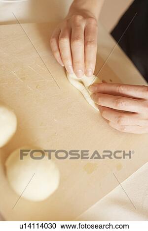 Stock Image - Woman making bagels, rolling dough, close up. Fotosearch