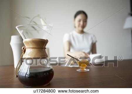 Stock Image - Woman sitting at table, drinking coffee, differential focus. Fotosearch