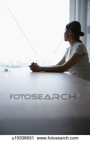 Stock Image - Woman sitting at table, looking away. Fotosearch