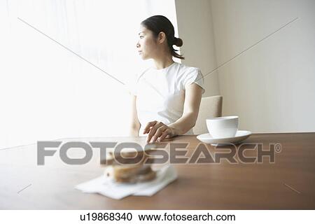 Stock Image - Woman sitting at table, looking away. Fotosearch