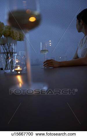 Stock Image - Woman sitting at table, wineglasses on table, differential focus. Fotosearch