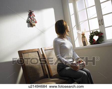 Woman sitting on chair by window, holding Christmas present View Large Photo Image Picture - Woman sitting on chair by window, holding Christmas present. Fotosearch