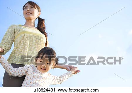 Stock Image - Woman with daughter smiling under sky. Fotosearch