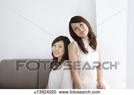 Stock Image - Women sitting on sofa looking at camera. Fotosearch
