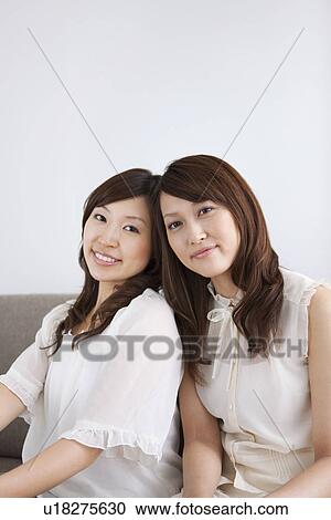 Stock Image - Women sitting on sofa looking at camera. Fotosearch
