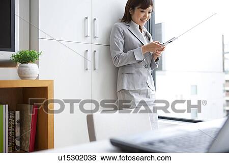 Young businesswoman looking at mobile phone by window View Large Photo Image Stock Photo - Young businesswoman looking at mobile phone by window. Fotosearch