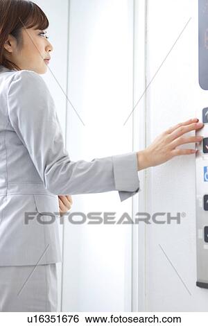 Stock Photograph - Young businesswoman pushing elevator button. Fotosearch