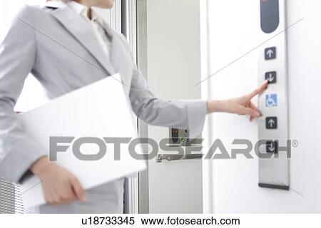Stock Photography - Young businesswoman pushing elevator button. Fotosearch