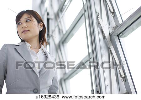 Stock Photograph - Young businesswoman standing by window, looking away. Fotosearch