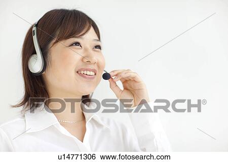 Stock Photograph - Young businesswoman wearing headset, smiling, white background. Fotosearch