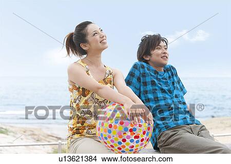 Young couple sitting at beach, woman holding beach ball View Large Photo Image Picture - Young couple sitting at beach, woman holding beach ball. Fotosearch