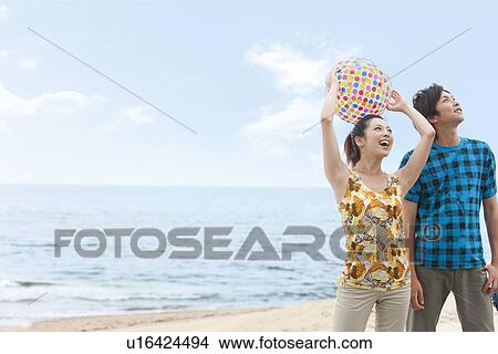 Picture - Young couple standing at beach, woman holding beach ball. Fotosearch