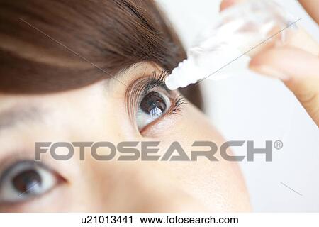 Stock Image - Young woman applying eye drops, close up. Fotosearch
