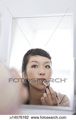 Stock Image - Young woman applying lipstick. Fotosearch
