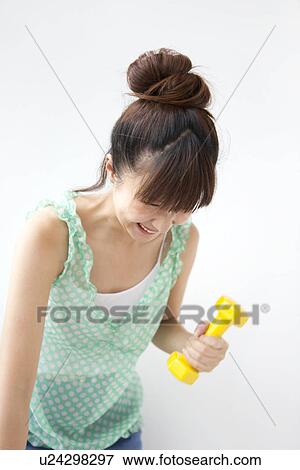 Stock Photo - Young woman doing exercise, using dumbbells, white background. Fotosearch