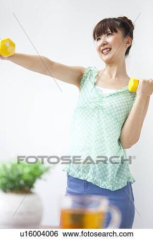 Stock Photograph - Young woman doing exercise, using dumbbells, white background. Fotosearch