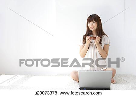 Stock Photo - Young woman holding cup of tea, looking away, white background. Fotosearch