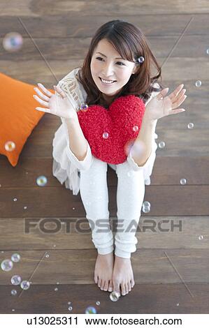 Stock Image - Young woman sitting on floor, soap bubbles over woman. Fotosearch