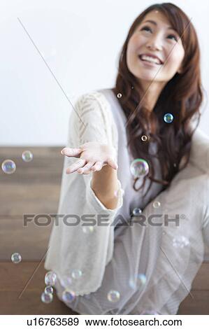 Stock Photo - Young woman sitting on floor, soap bubbles over woman. Fotosearch