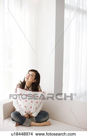 Young woman sitting on sofa, looking up View Large Photo Image Picture - Young woman sitting on sofa, looking up. Fotosearch