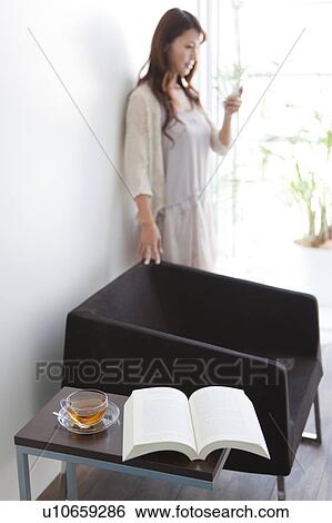 Young woman standing by sofa, looking at mobile phone View Large Photo Image Stock Photograph - Young woman standing by sofa, looking at mobile phone. Fotosearch