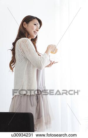 Young woman standing by window, holding cup of tea View Large Photo Image Stock Image - Young woman standing by window, holding cup of tea. Fotosearch